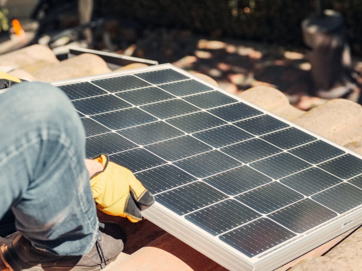 A worker installs a solar panel on a sunlit rooftop, exemplifying renewable energy.